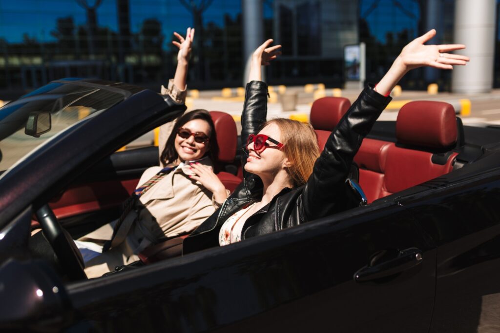 two-cheerful-girls-joyfully-spending-time-together-driving-cabriolet-car-city-streets-outdoor